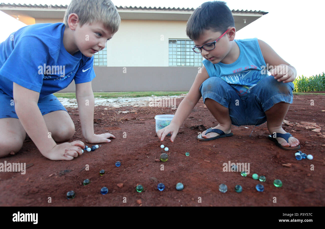 Apesar de toda a tecnologia disponível e de fácil acesso em Campo Mourão, na Região Centro-Oeste do Paraná, o jogo de bolinha de gude ainda fascina crianças do interior. Na foto, os estudantes Guilherme e Vitor disputam uma partida de bolinha de gude em um triângulo desenhado na terra, na casa dos avós de Guilherme. Stock Photo