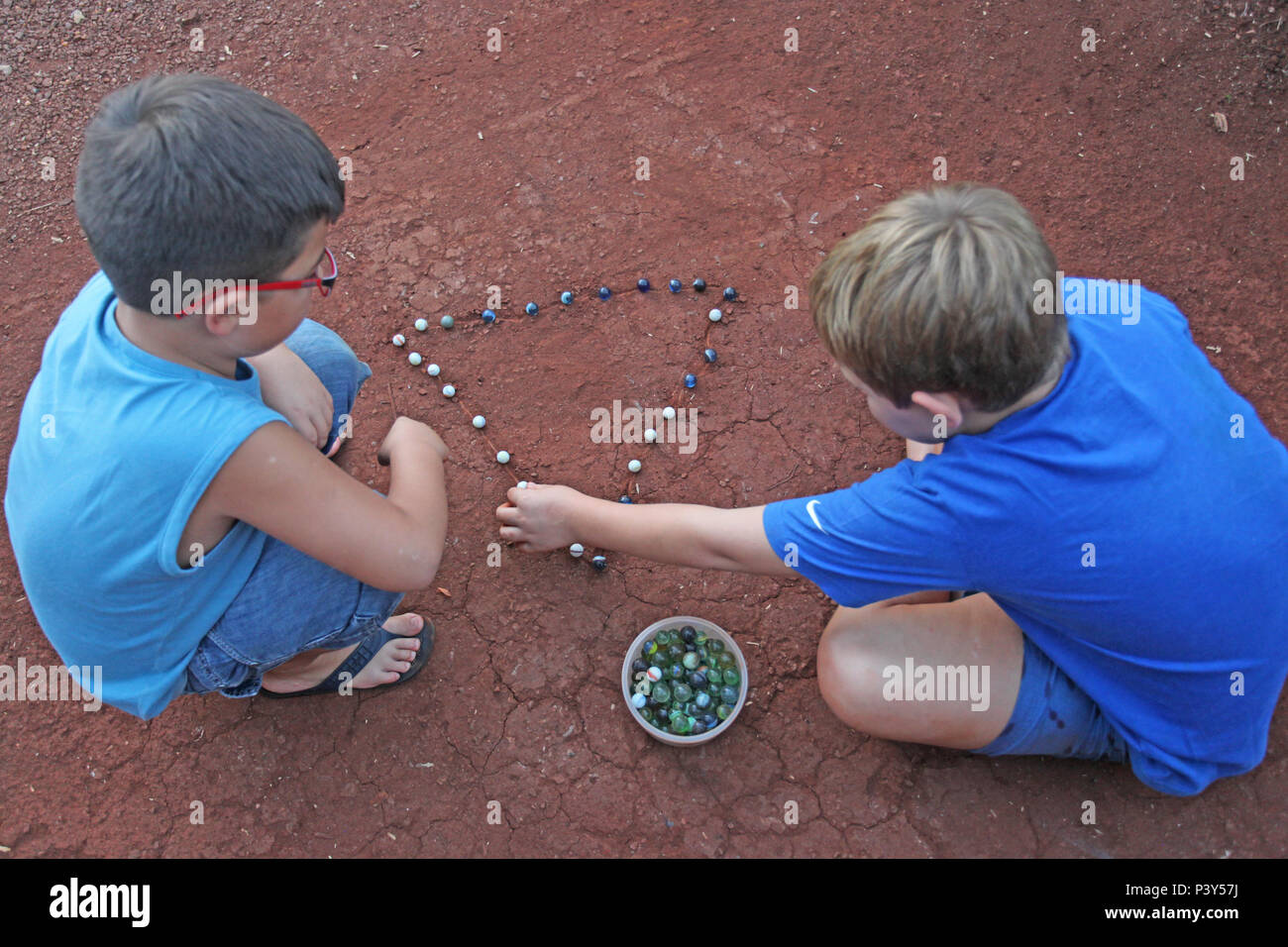 Apesar de toda a tecnologia disponível e de fácil acesso em Campo Mourão, na Região Centro-Oeste do Paraná, o jogo de bolinha de gude ainda fascina crianças do interior. Na foto, os estudantes Guilherme e Vitor disputam uma partida de bolinha de gude em um triângulo desenhado na terra, na casa dos avós de Guilherme. Stock Photo