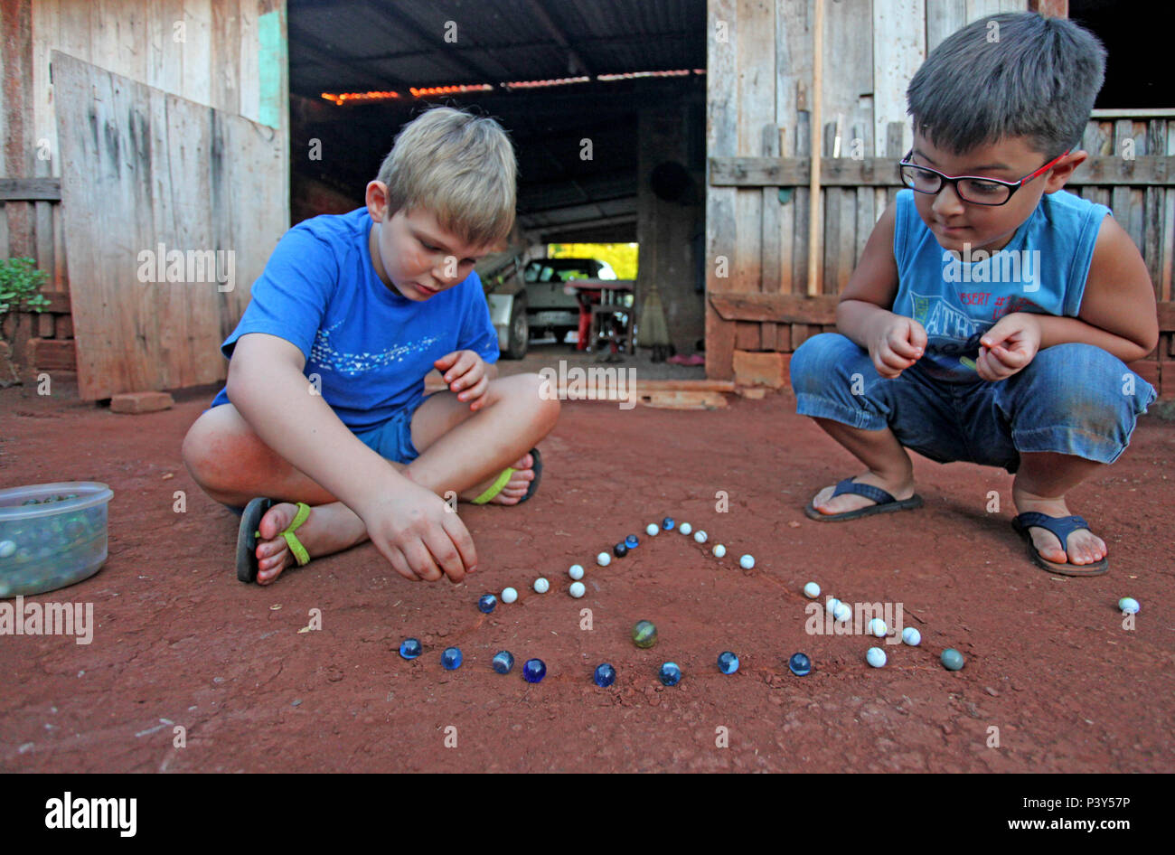 Apesar de toda a tecnologia disponível e de fácil acesso em Campo Mourão, na Região Centro-Oeste do Paraná, o jogo de bolinha de gude ainda fascina crianças do interior. Na foto, os estudantes Guilherme e Vitor disputam uma partida de bolinha de gude em um triângulo desenhado na terra, na casa dos avós de Guilherme. Stock Photo