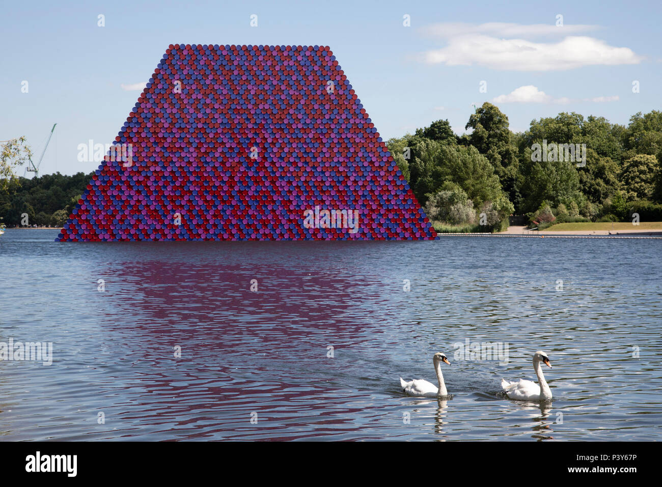 Art installation The Mastaba, by artist Christo, installed on the Serpentine lake in Hyde Park on June 18th 2018 in London, United Kingdom. The sculpture consists of 7,506 stacked barrels, painted in shades of red, white, blue and mauve. The completed piece forms part of an exhibition by Christo and his late wife, Jeanne-Claudes work, entitled Christo and Jeanne-Claude: Barrels and The Mastaba 19582018 to be held at The Serpentine Gallery. Stock Photo