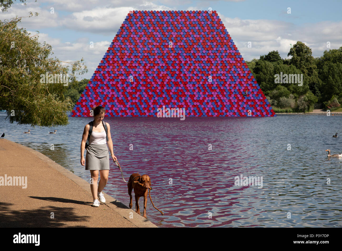 Art installation The Mastaba, by artist Christo, installed on the Serpentine lake in Hyde Park on June 18th 2018 in London, United Kingdom. The sculpture consists of 7,506 stacked barrels, painted in shades of red, white, blue and mauve. The completed piece forms part of an exhibition by Christo and his late wife, Jeanne-Claudes work, entitled Christo and Jeanne-Claude: Barrels and The Mastaba 19582018 to be held at The Serpentine Gallery. Stock Photo