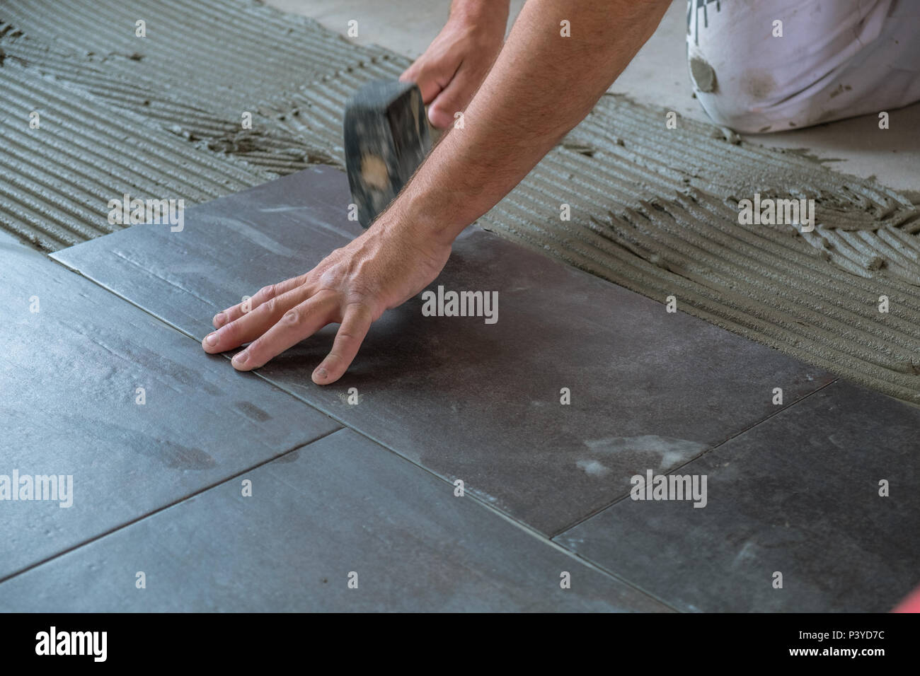 Worker placing ceramic floor tiles on adhesive surface, leveling with