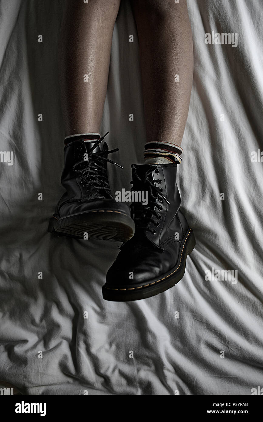Top down shot of a teengirl's legs chilling in bed wear her black dr marten shoes being a rebel Stock Photo