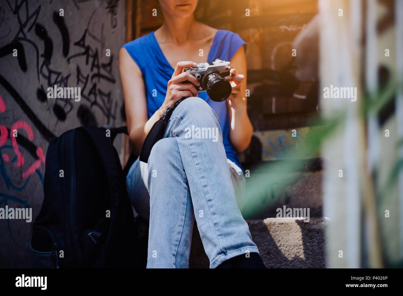 Young woman sitting on stairs, holding vintage camera and looking to the photos made in the city tour Stock Photo