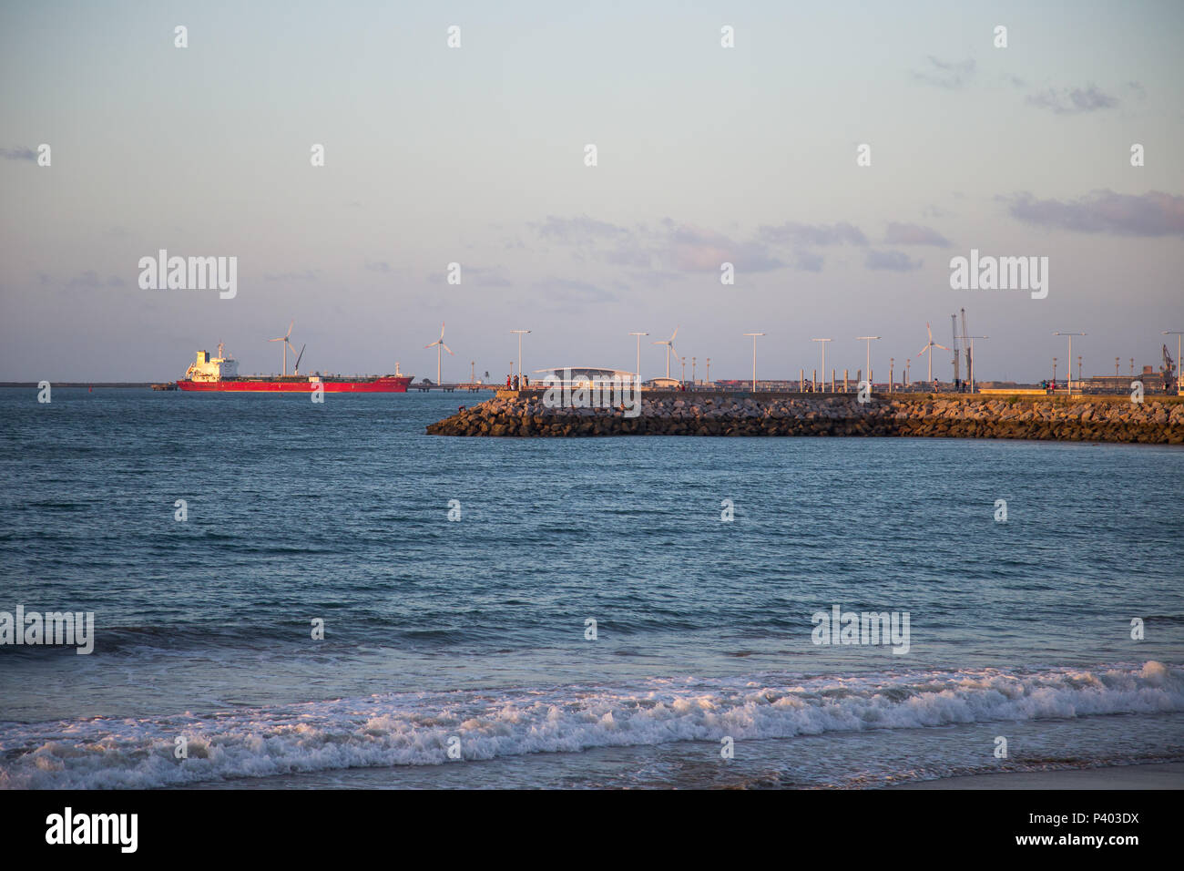 Vista do quebra mar na praia do Meireles, em Fortaleza, CE, Brasil. Ao fundo um navio e hélices de turbinas eólicas. Stock Photo