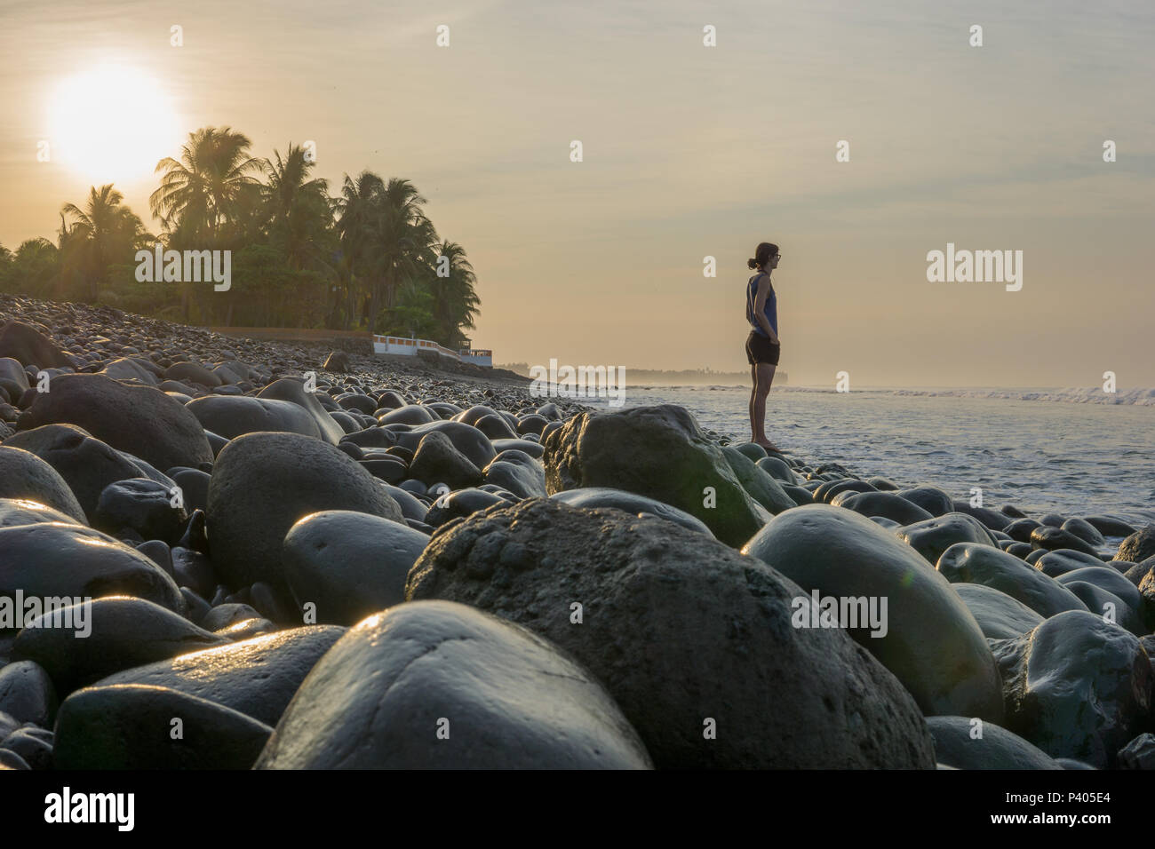 Young woman standing on rock near sea looking at the waves. Stock Photo