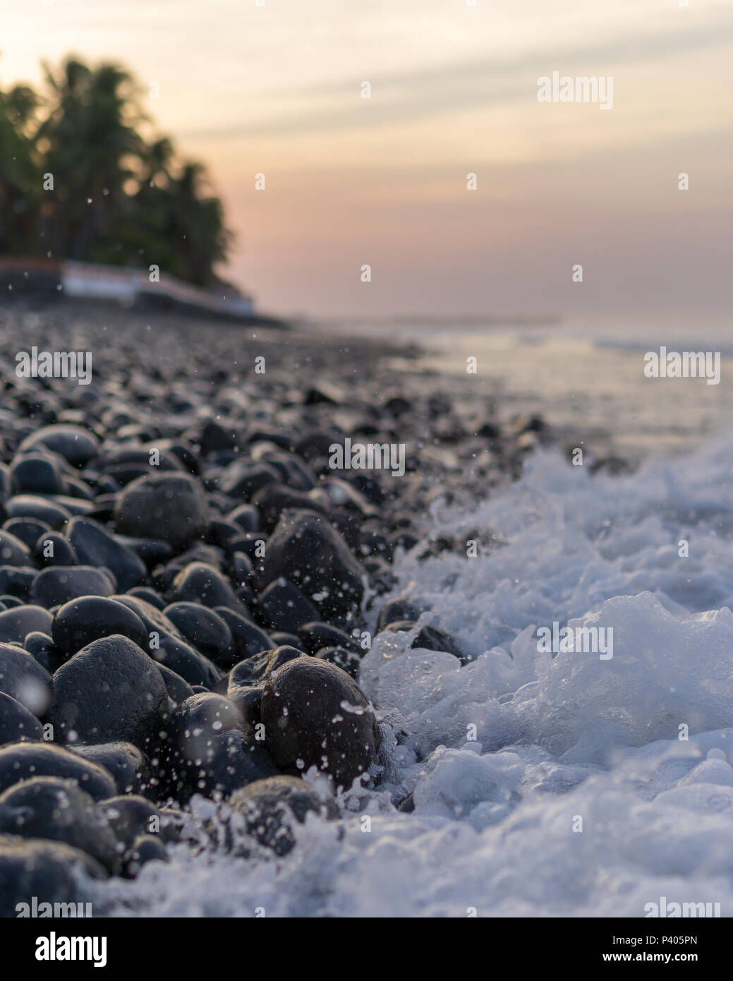 Ocean splash with a lot of foam on dark rocks at sunrise. Stock Photo
