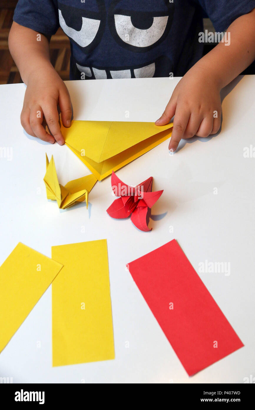 Brincadeiras dentro de casa. Criança faz origami, dobraduras de papel de  origem japonesa Stock Photo - Alamy