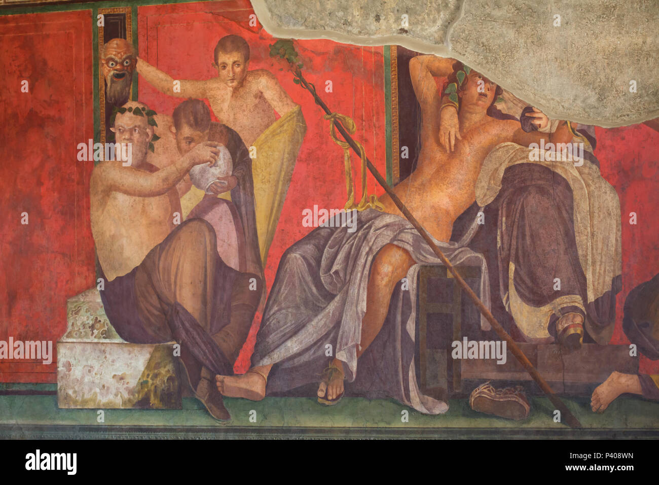 Dionysian Mysteries (Bacchian Mysteries) depicted in the Roman fresco in the triclinium (Roman dining room) in the Villa of the Mysteries (Villa dei Misteri) in the archaeological site of Pompeii (Pompei) near Naples, Campania, Italy. Initiation rite from the mysterious cult of Dionysus (Bacchus) is probably depicted in the murals. This fresco shows a young satyr being offered a bowl of wine by Silenus while behind him, another satyr holds up a frightening mask which the drinking satyr sees reflected in the bowl. Next to them sits a goddess (Ariadne or Semele), with Dionysus (Bacchus) lying ac Stock Photo