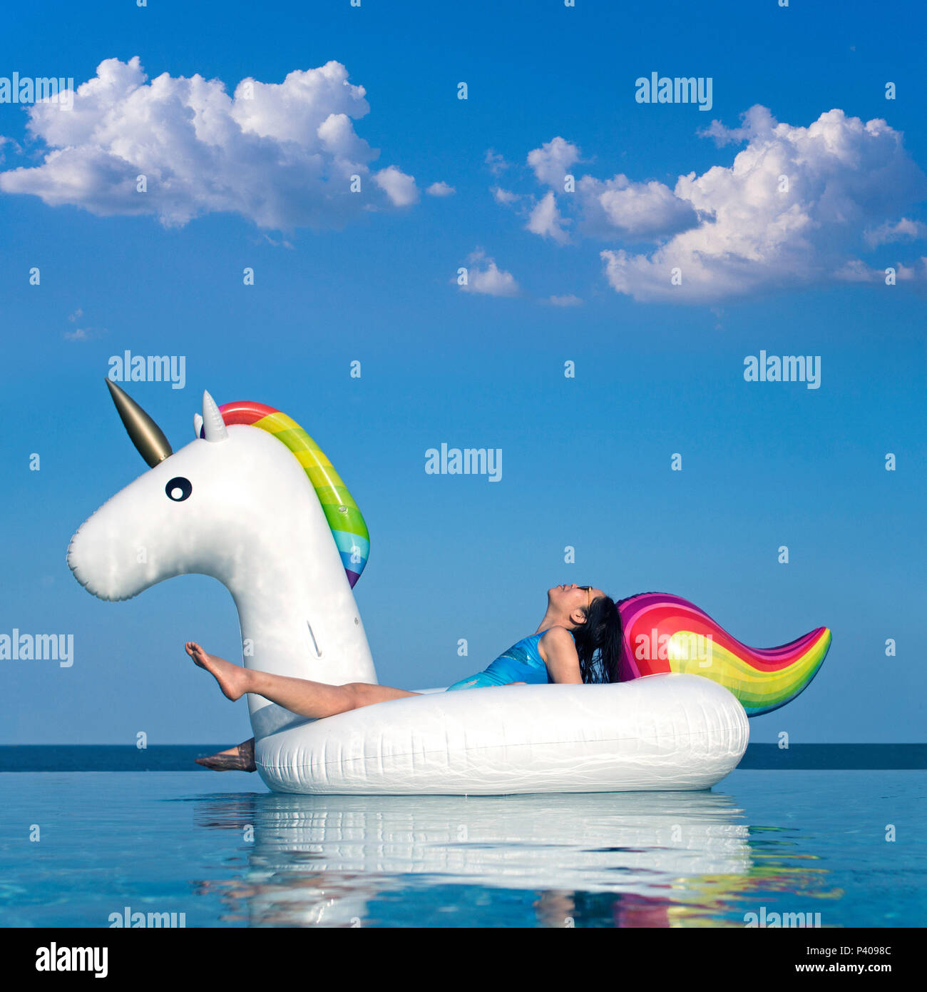 Woman Relaxing on Inflatable Rainbow Unicorn in Swimming Pool Stock Photo