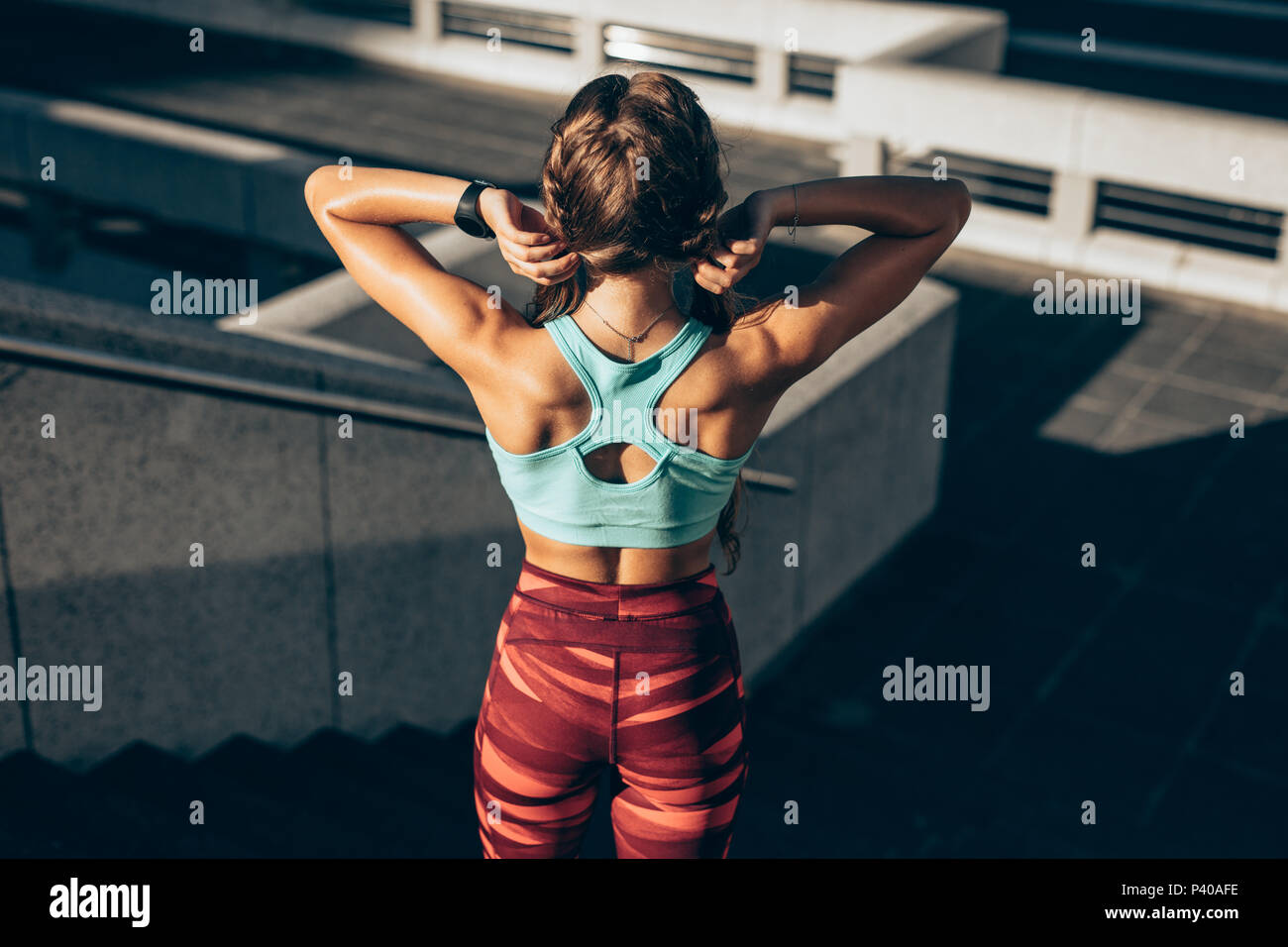 Rear view of fit young woman in sports clothing standing on steps in morning. Female with muscular body ready for workout outdoors. Stock Photo