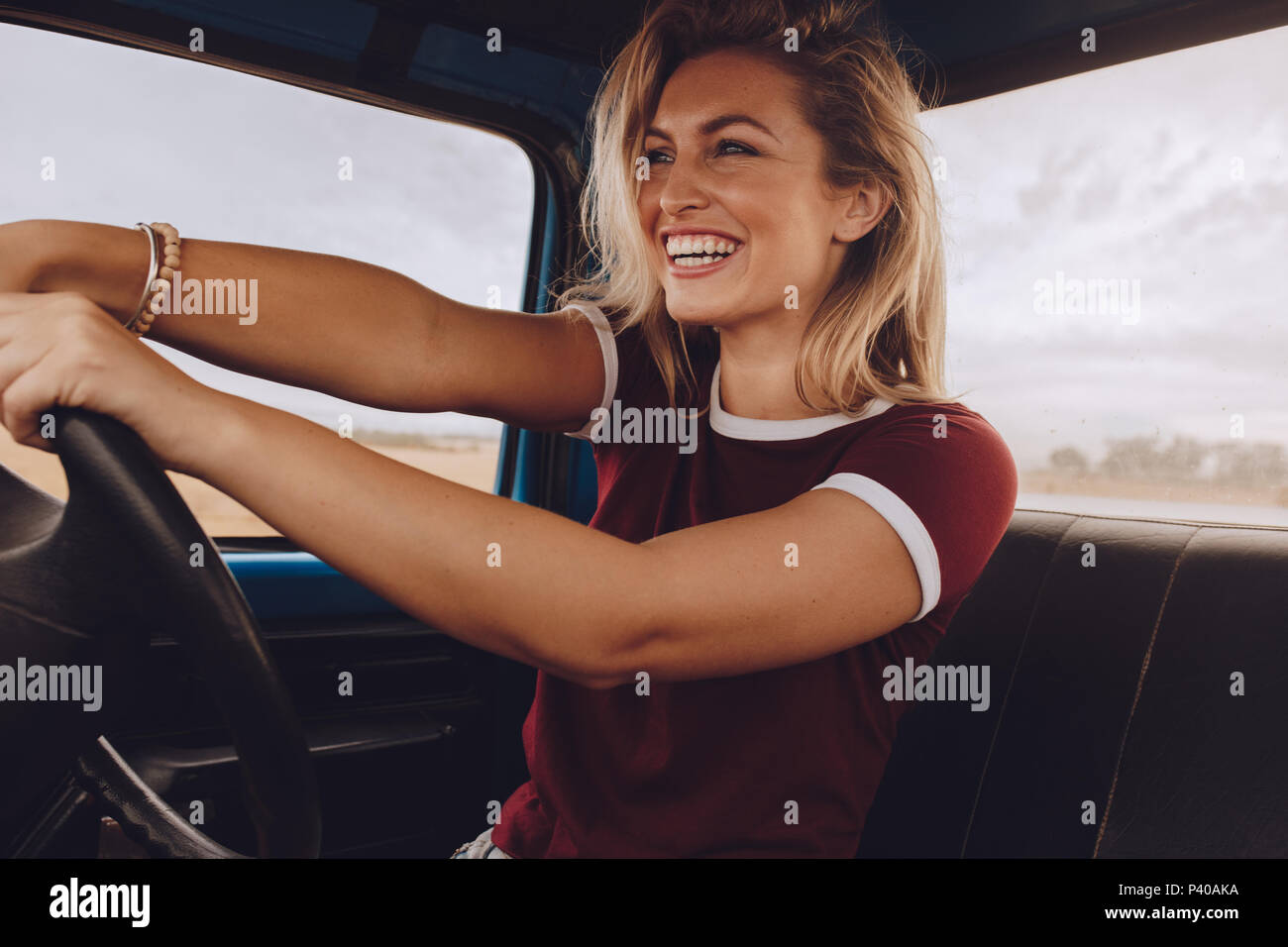 Smiling woman enjoying driving a car. Cheerful female going on a road trip by a old truck. Stock Photo