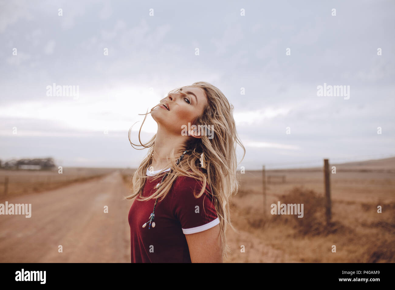 Attractive woman standing on country road. Female with blond hair standing outdoors in countryside. Stock Photo