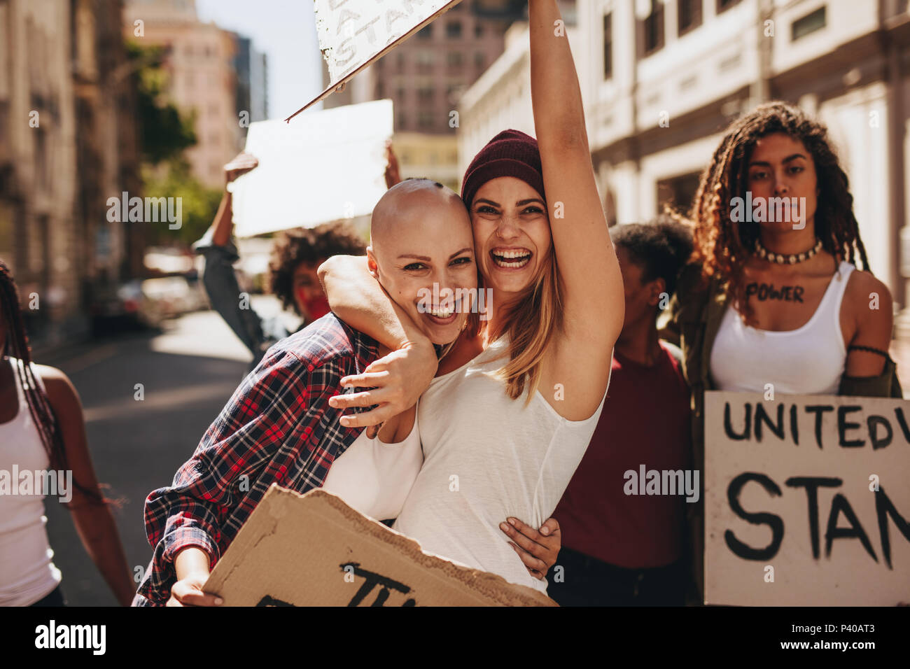 Young crowd demonstrating with signboard on road. Female activists enjoying at protest. Stock Photo