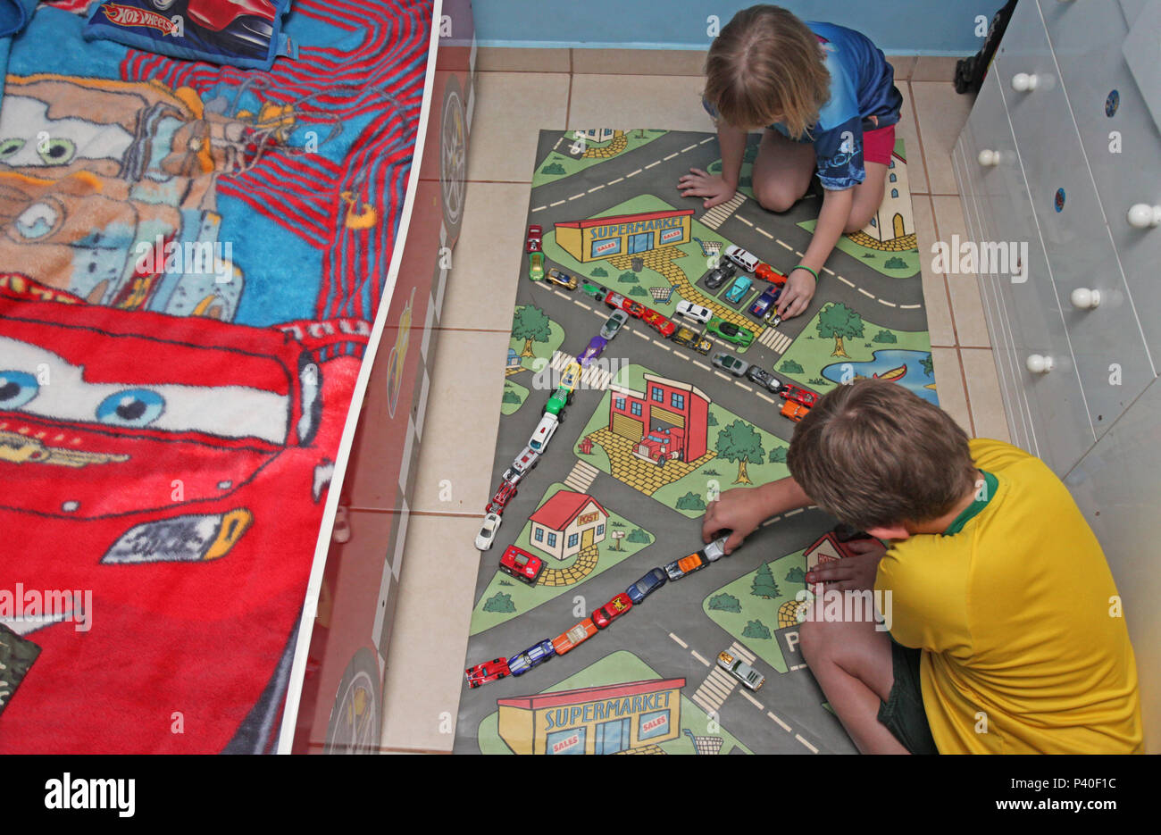 Crianças brincam em tapete temático simulando cãos no trânsito das cidades grandes. Na foto, menina e menino brincam com carrinhos em tapete temático, dentro do quarto da residência. Stock Photo