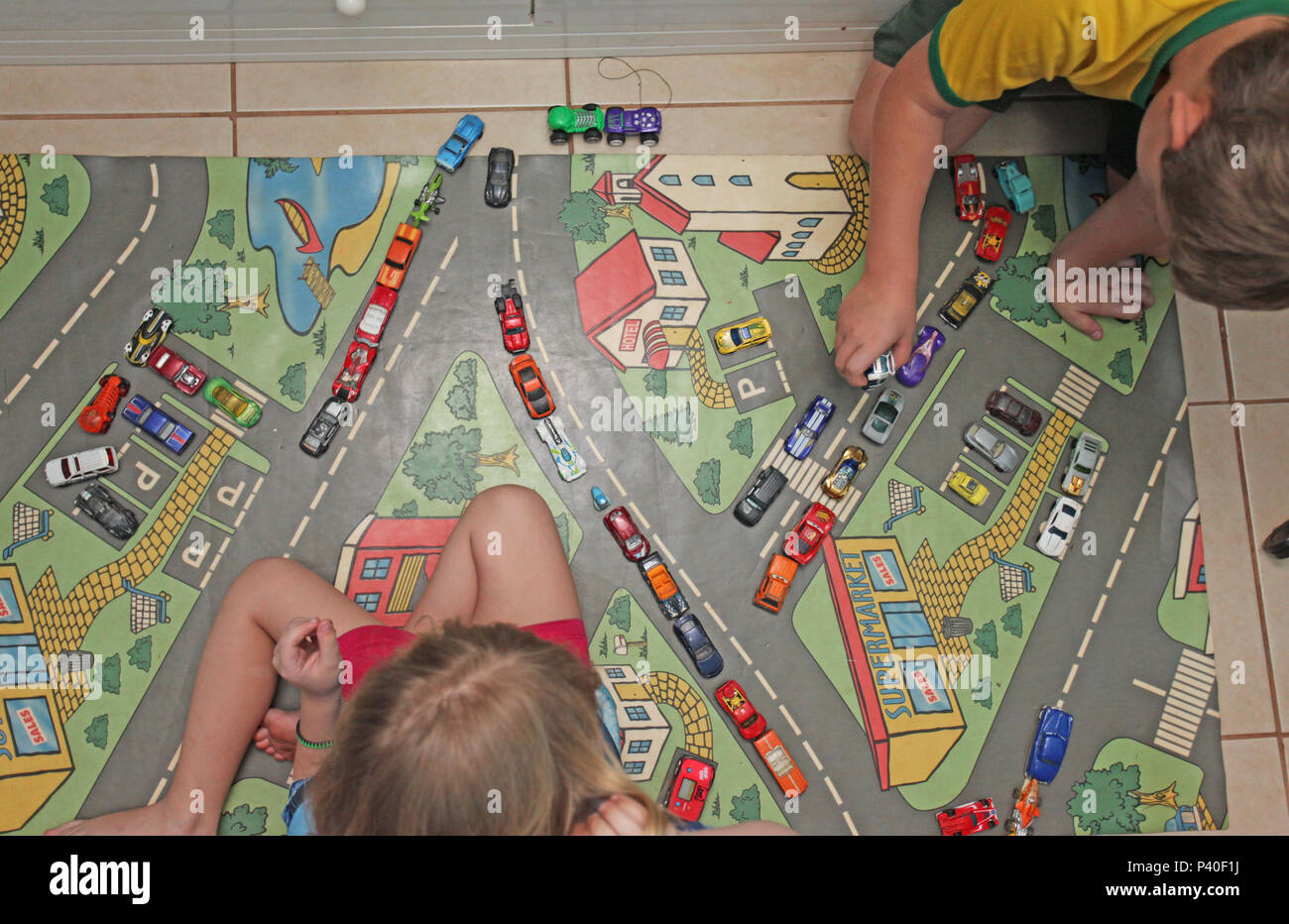Crianças brincam em tapete temático simulando cãos no trânsito das cidades grandes. Na foto, menina e menino brincam com carrinhos em tapete temático, dentro do quarto da residência. Stock Photo