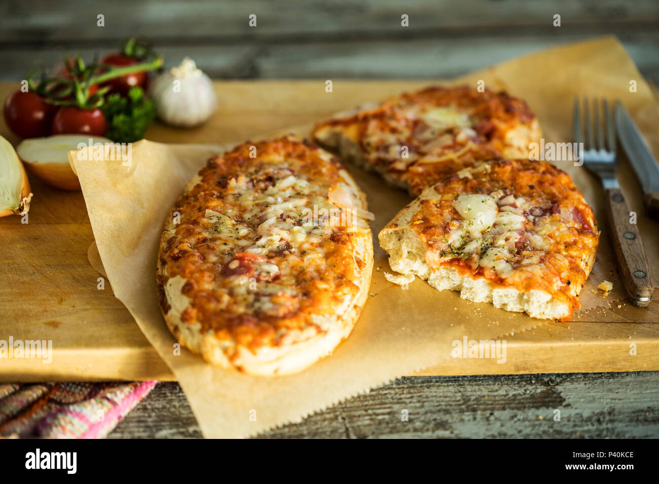 rustikales Pizzabrot mit Salami, Käse, Zwiebeln und Tomate, serviert auf Holzbrett Stock Photo
