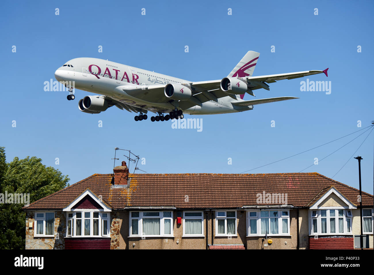 A Qatar Airways Airbus A380-800 aircraft, registration number A7-API, flying low over houses as it descends for a landing at Heathrow Airport, London. Stock Photo