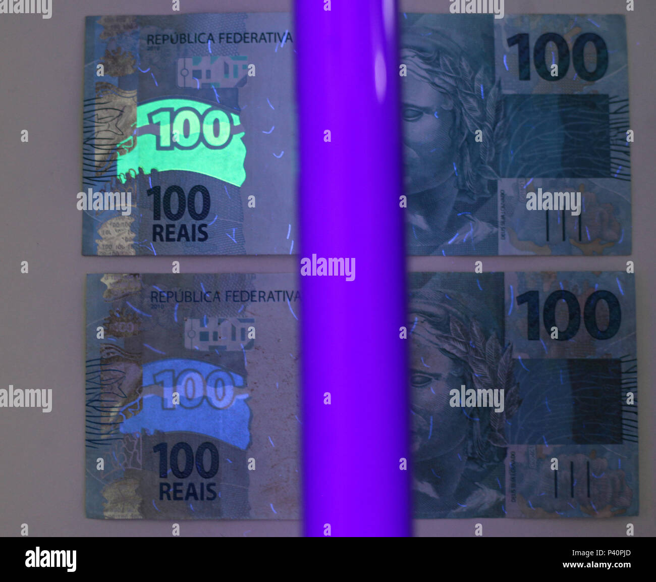 Nota falsa e verdadeira de R100,00. Na foto, luz negra incide em nota verdadeira deixando uma Nota falsa e verdadeira de R100,00. Na foto, luz negra incide em nota verdadeira deixando uma