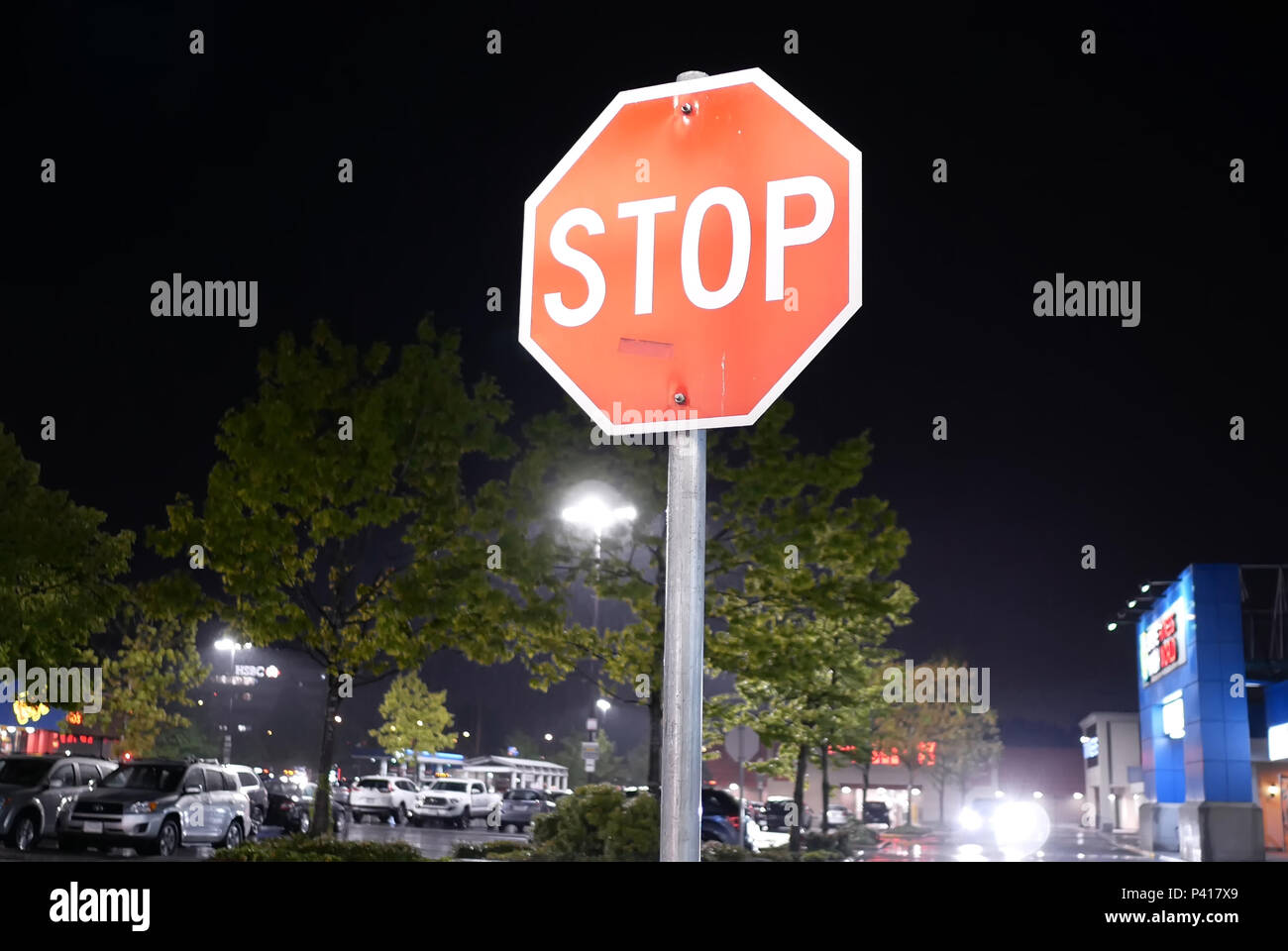 Coquitlam, BC, Canada - May 08, 2018 : Motion of stop sign in front of parking lot at raining night Stock Photo