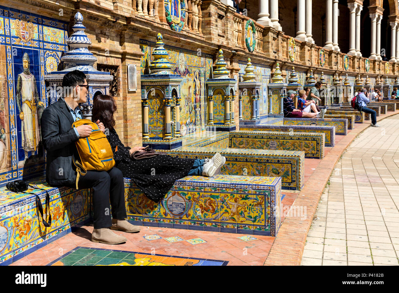 Tourists relaxing in the sun on the tiled province alcoves, Plaza de Espana, Andalusia, Spain. Stock Photo