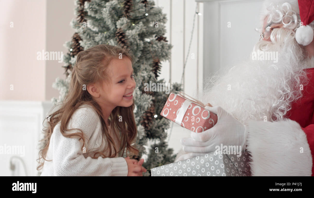 Santa Claus hugging a little cute girl and giving her Christmas present ...