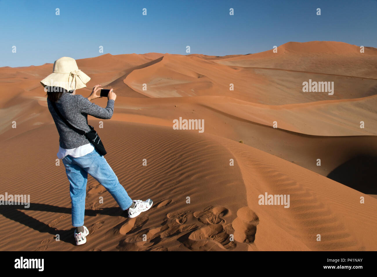 A tourist makes photos while hiking on the famous red sand dunes at ...