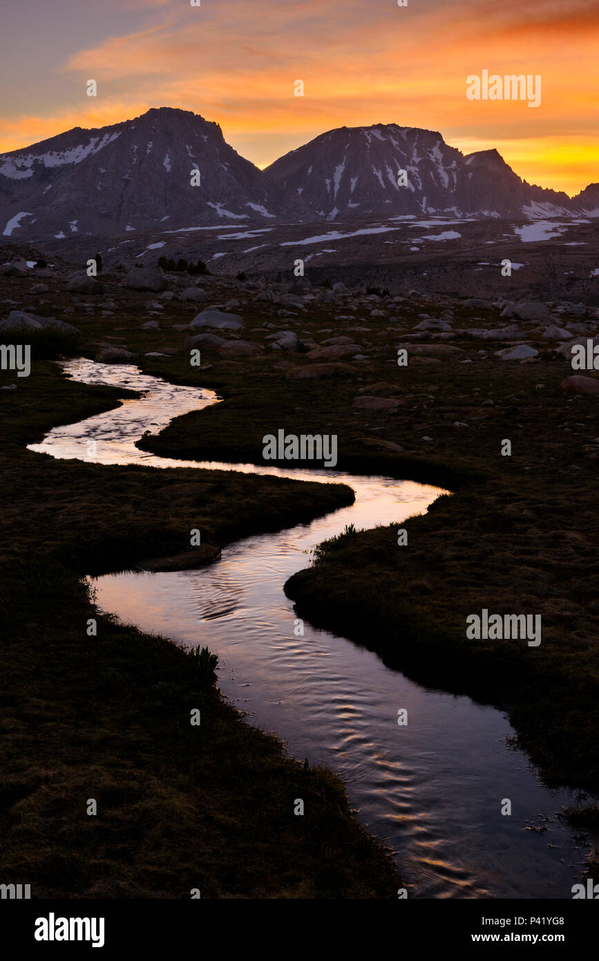 Sunset behind Merriam and Royce Peaks with mountain stream in the High Sierra mountains over Pine Creek Pass west of Bishop, California,USA. Stock Photo