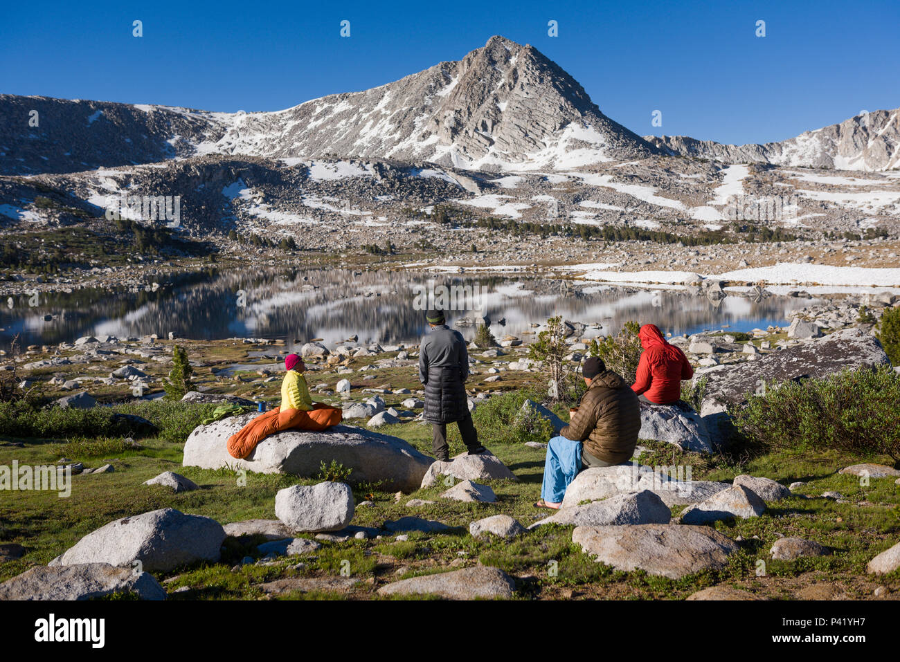 Backpackers drink coffee at sunrise at L Lake in the High Sierra mountains over Pine Creek Pass west of Bishop, California, July 2016. Stock Photo