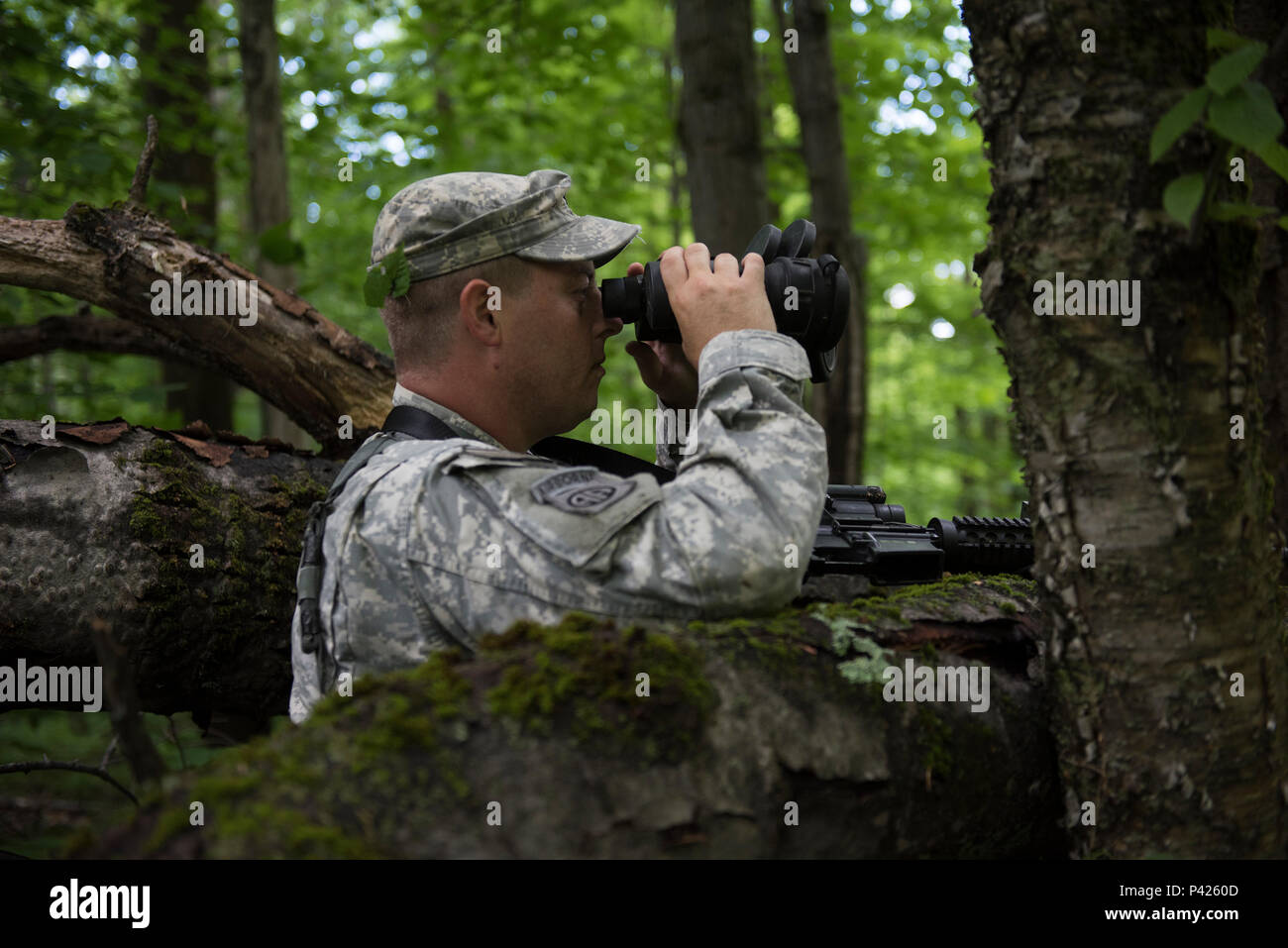 U.S. Army Sgt. Graham Skinner, a scout with Headquarters, Headquarters Company, 3rd Battalion, 172nd Infantry Regiment (Mountain), Vermont National Guard, monitors opposition forces during a reconnaissance training mission on Camp Ethan Allen Training Site, Jericho, Vt., June 6, 2016. Skinner’s company is participating in multiple training events over the next two weeks as part of their annual training. (U.S. Air National Guard photo by Tech. Sgt. Sarah Mattison/Released) Stock Photo
