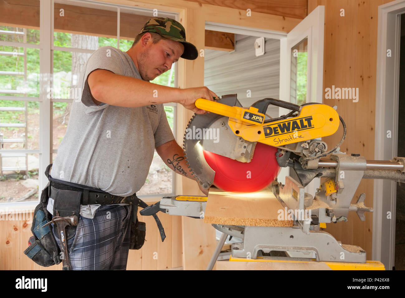 A construction worker using a circular saw to cut a wooden plank in Ontario, Canada. Stock Photo