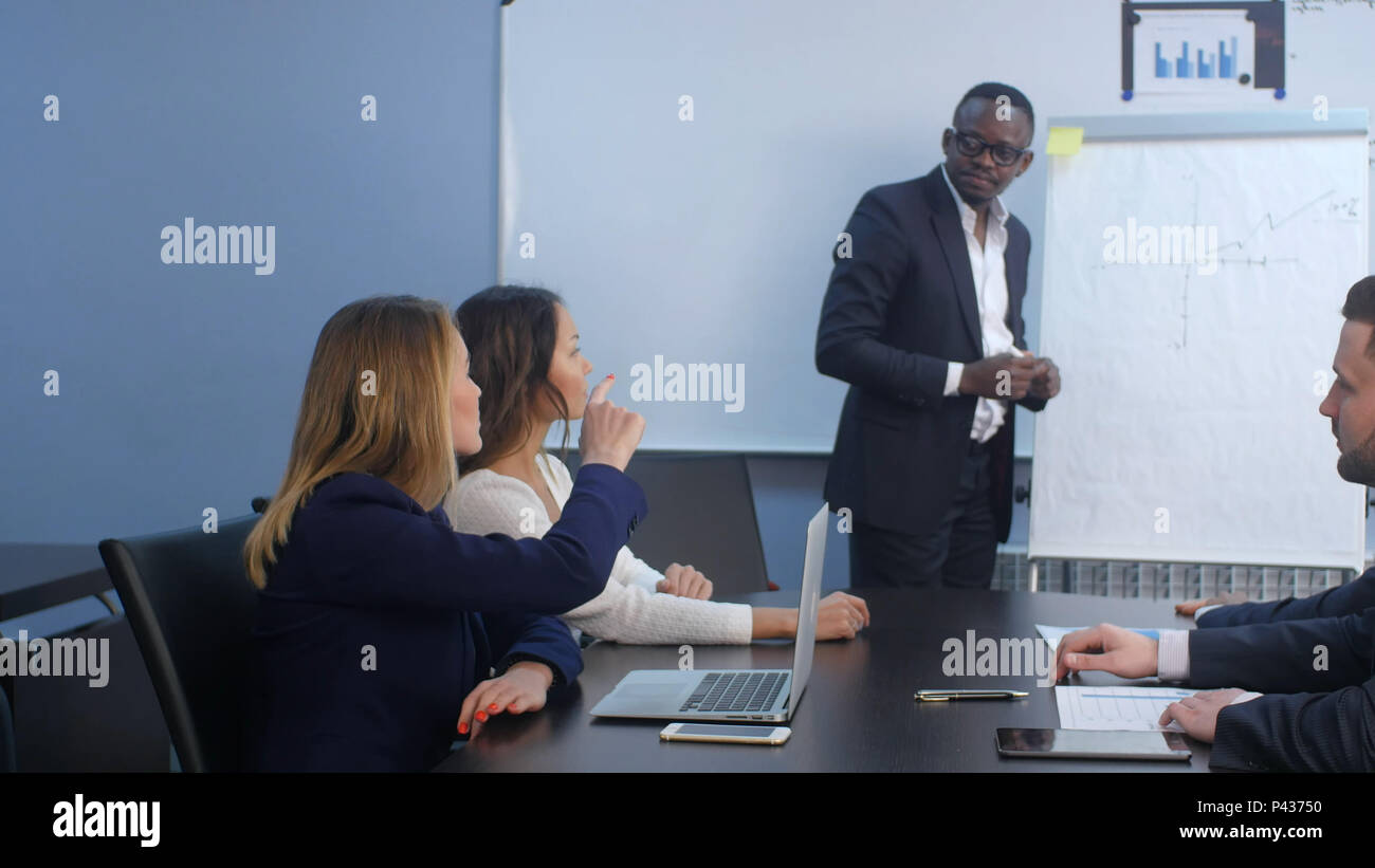 Colleagues asking a question to a businesswoman during a presentation Stock Photo