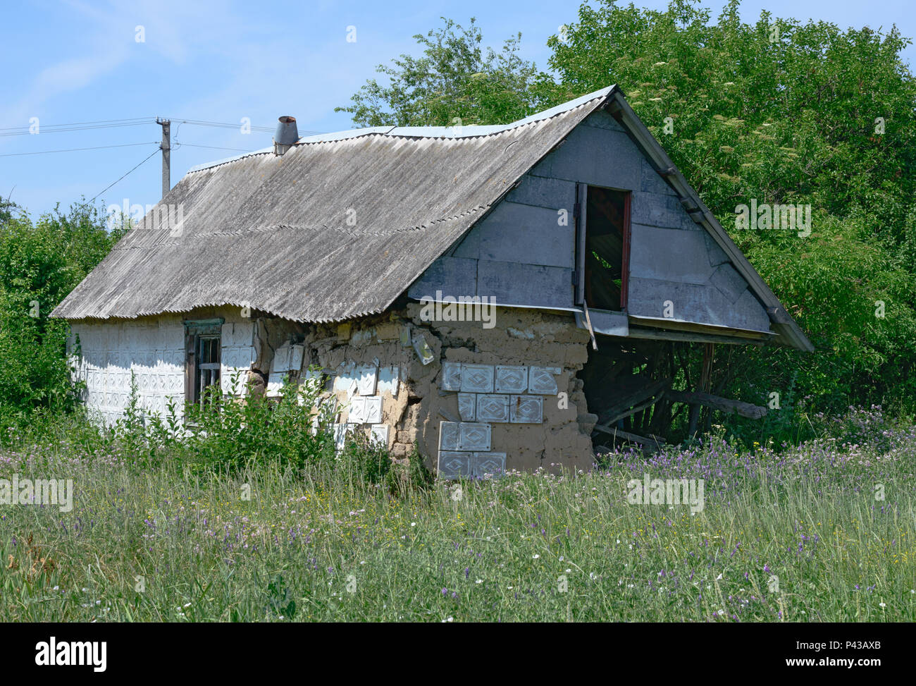 Abandoned small rural hut  with completely ruined corner in bright summer sunlight in Ukraine. Stock Photo