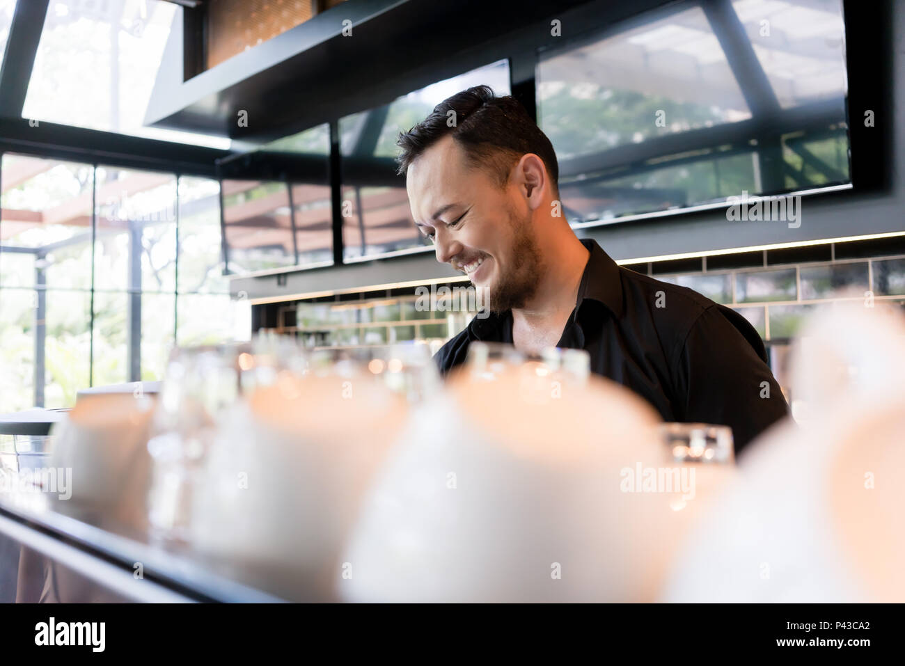 Happy young man working as barista behind the bar counter Stock Photo