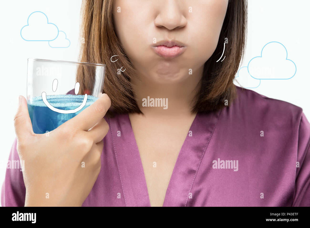 Asian woman rinsing and gargling while using mouthwash from a glass against gray background. Dental Healthcare Concepts. Stock Photo