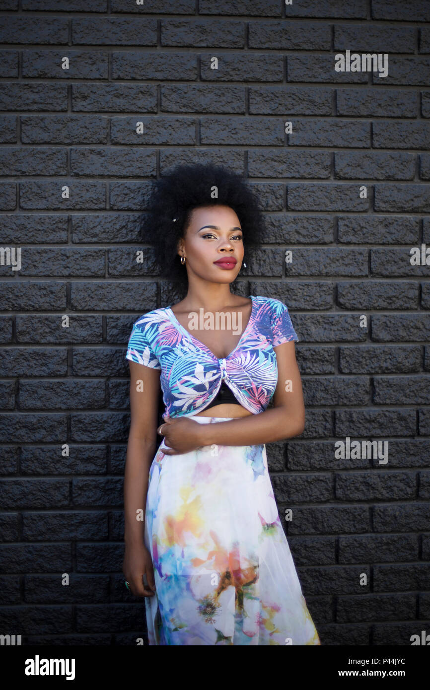 A young african model stands with her arm across her midriff against a darkly painted wall Stock Photo