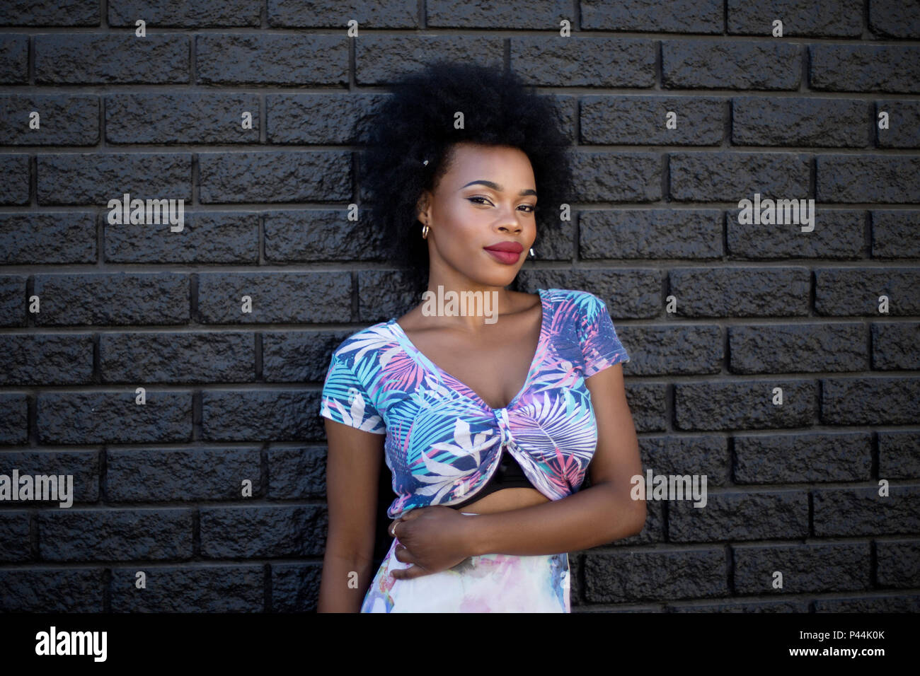A young african model stands with her arm across her midriff against a darkly painted wall Stock Photo