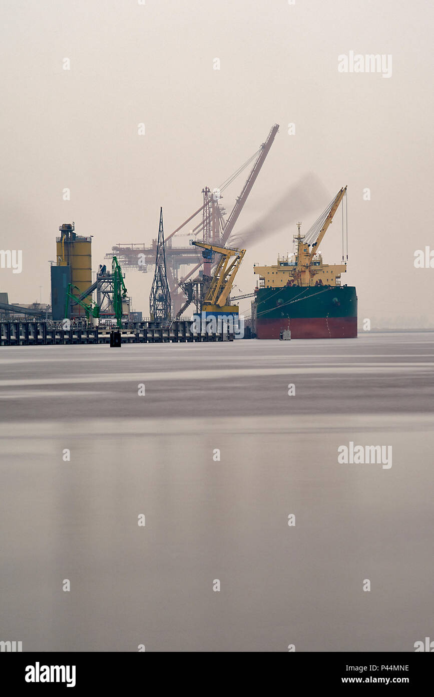 Container ship docked in the port of Amsterdam being unloaded by huge cranes on the shore Stock Photo