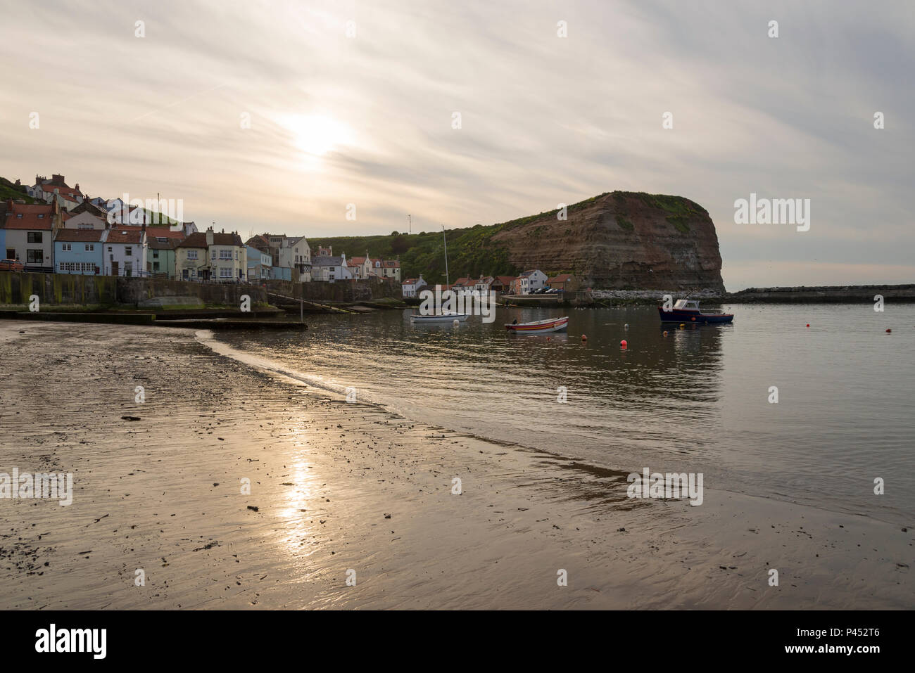 Beautiful May evening in the picturesque village of Staithes, North Yorkshire. The sun setting in a sky of high cloud above the harbour. Stock Photo