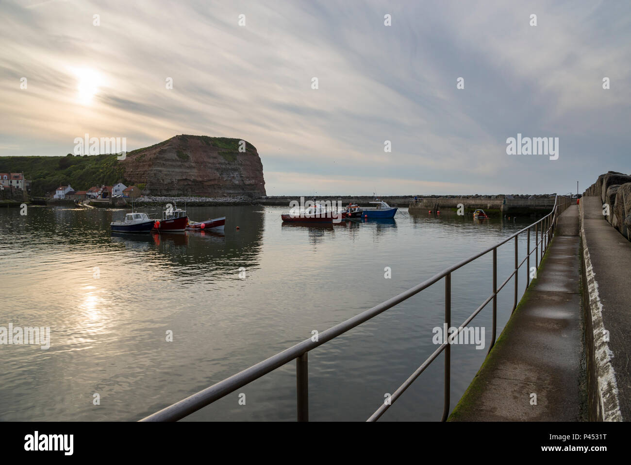 Beautiful May evening in the picturesque village of Staithes, North Yorkshire. The sun setting in a sky of high cloud above the harbour. Stock Photo