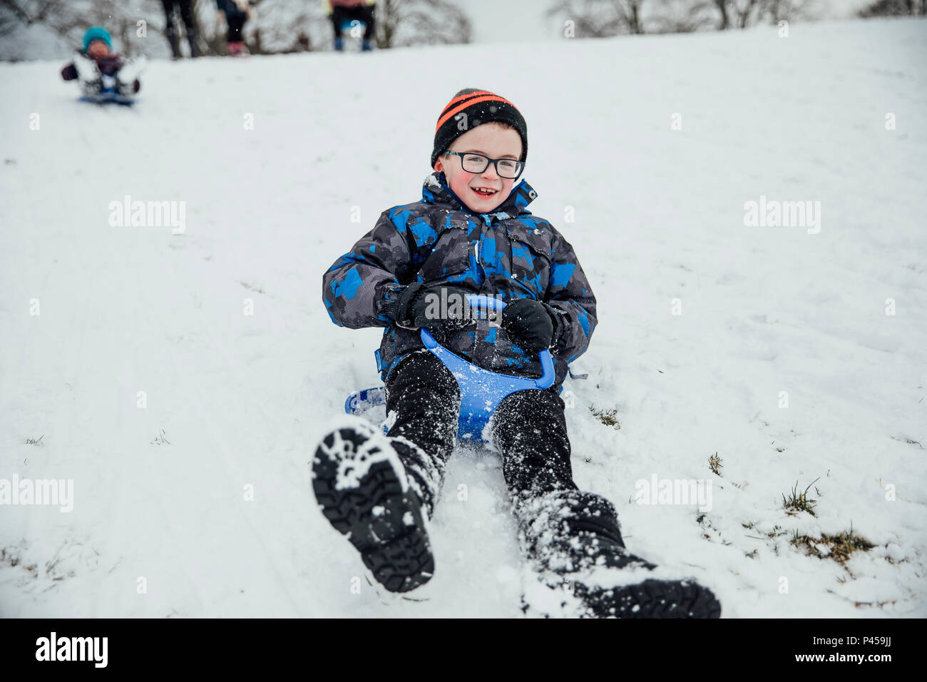Happy toddler boy sliding down snow in the mountains stock photo