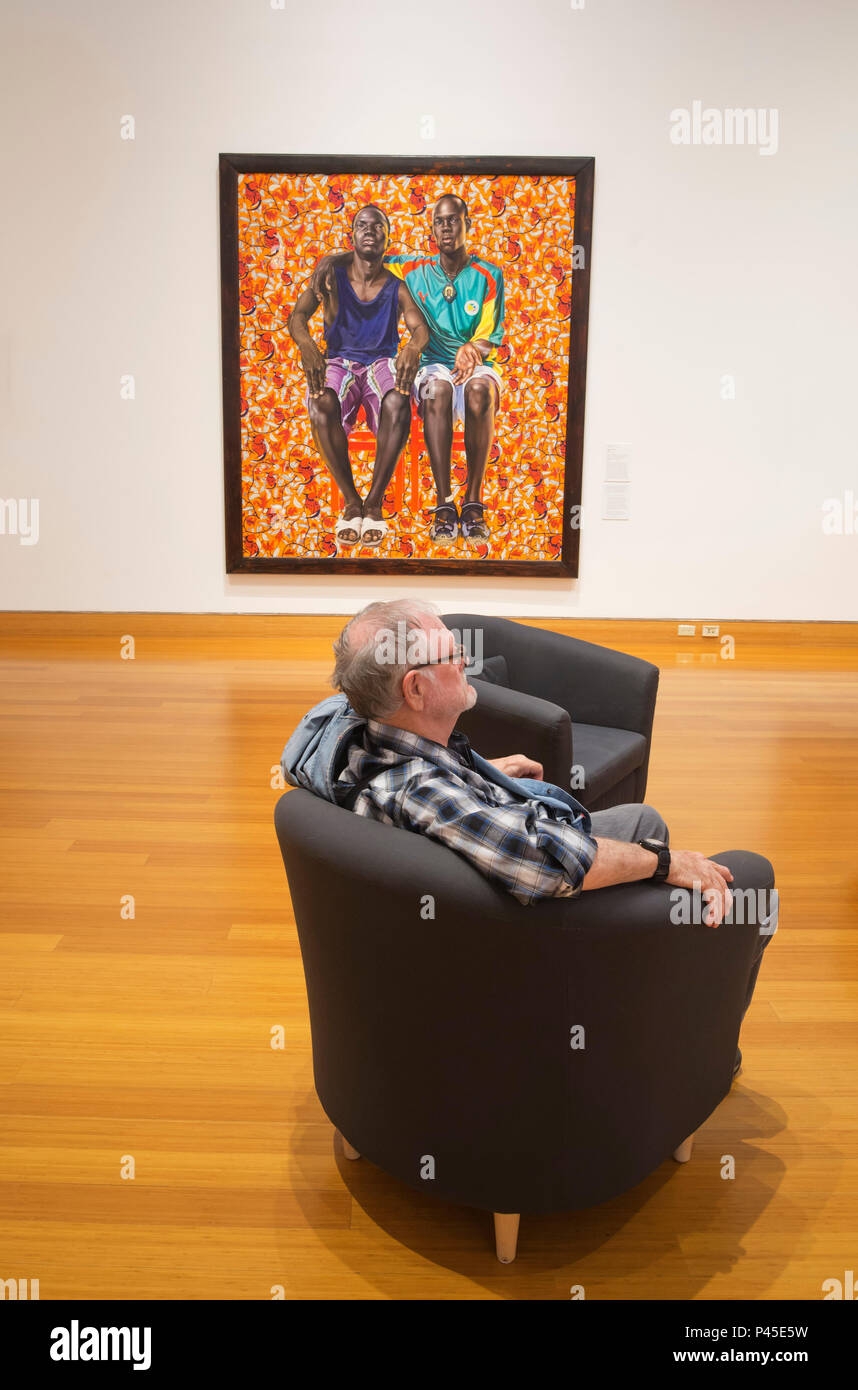 Painting 'Dogon Couple' by contemporary African-American artist Kehinde Wiley is on display. Man relaxing in chair with painting in background. Stock Photo