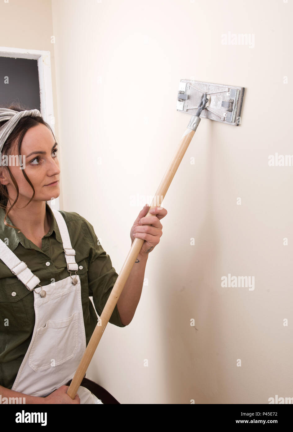 Young Woman Is Sanding Wall With Pole Sander Before Painting In