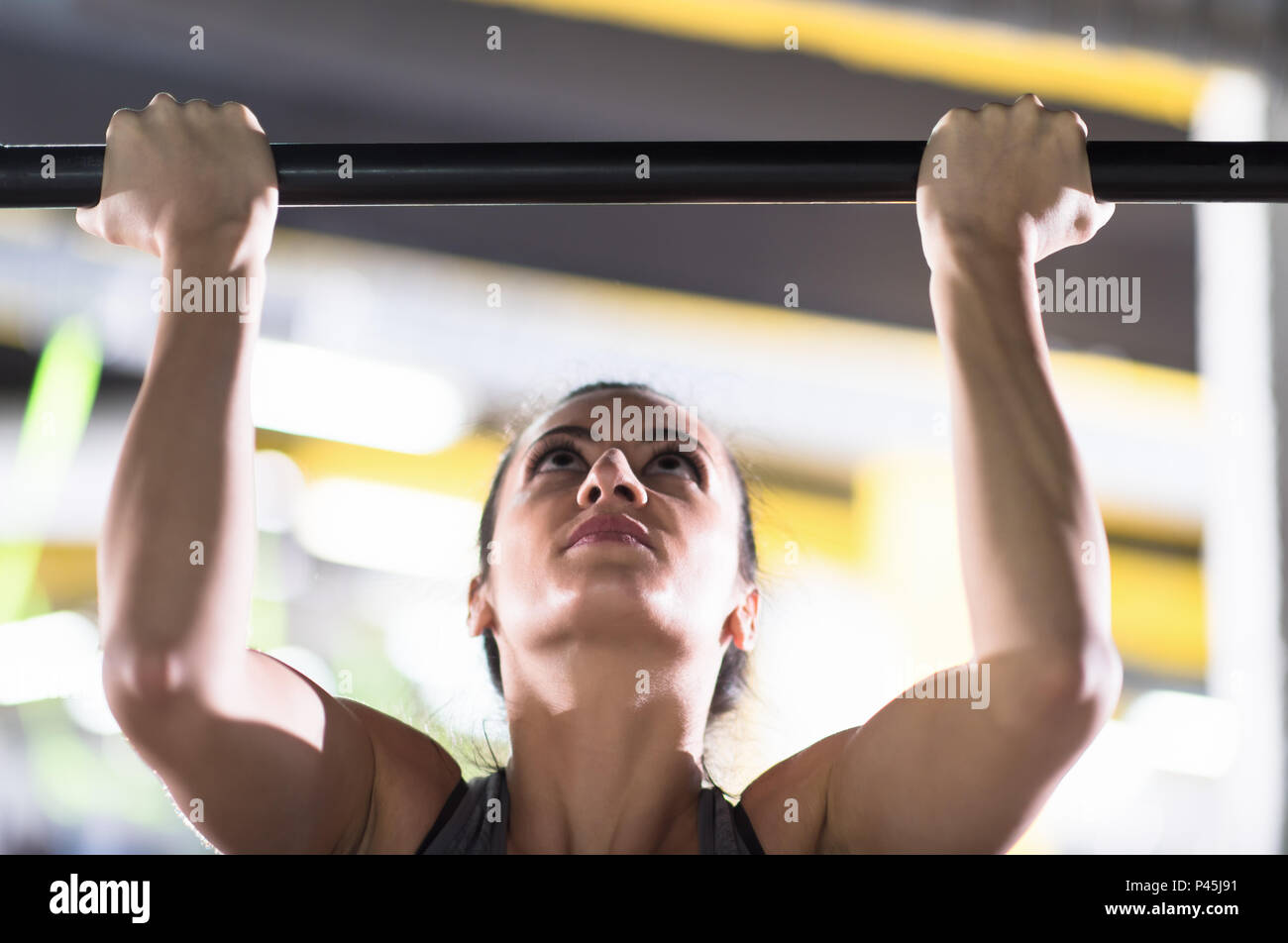 young muscular woman doing pull ups on the horizontal bar as part of ...