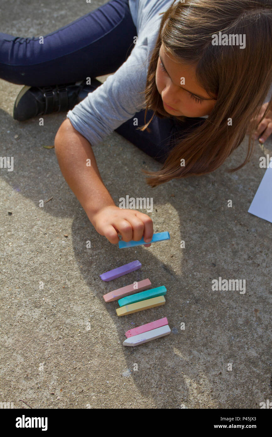 Girl kid thinking, writing and counting on mathematical equations with colored chalks on a pavement. School and vacation concept. Education concept. S Stock Photo