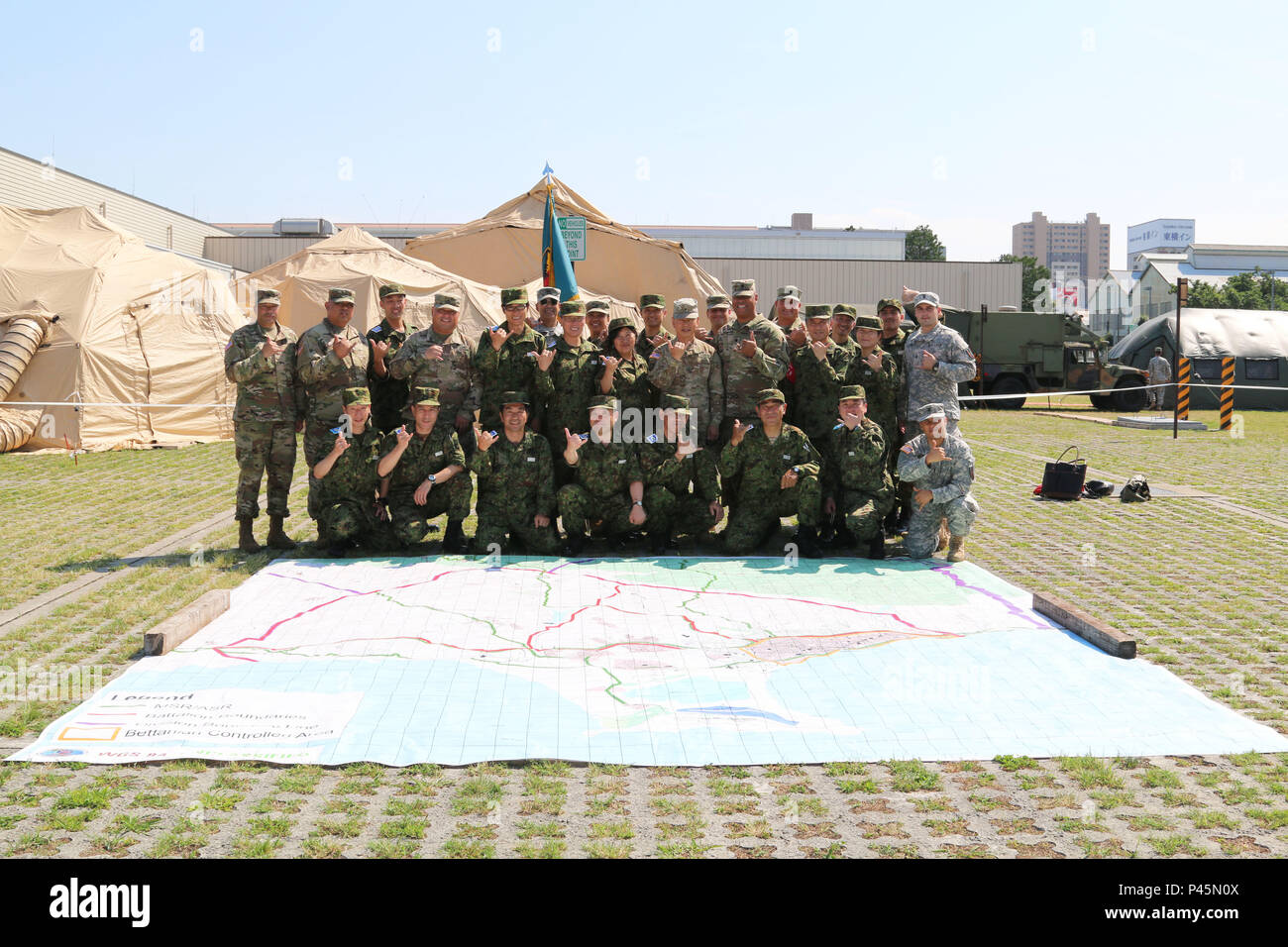 U.S. and Japan Ground Self-Defense Force (JGSDF) service members pose for a photo behind a 30 by 30 feet map outside Sagamihara Depot Mission Training Complex during exercise Imua Dawn 2016, Sagamihara, Japan, June 18, 2016.  Imua Dawn 2016 provides opportunities for U.S. and Japanese forces to come together and train for potential real world events, better preparing them in supporting regional populations in all Humanitarian Assistance and Disaster Relief (HADR) and Noncombatant Evacuation Operations (NEO). Training together, the U.S. and Japan Ground Self-Defense Force can further develop ta Stock Photo