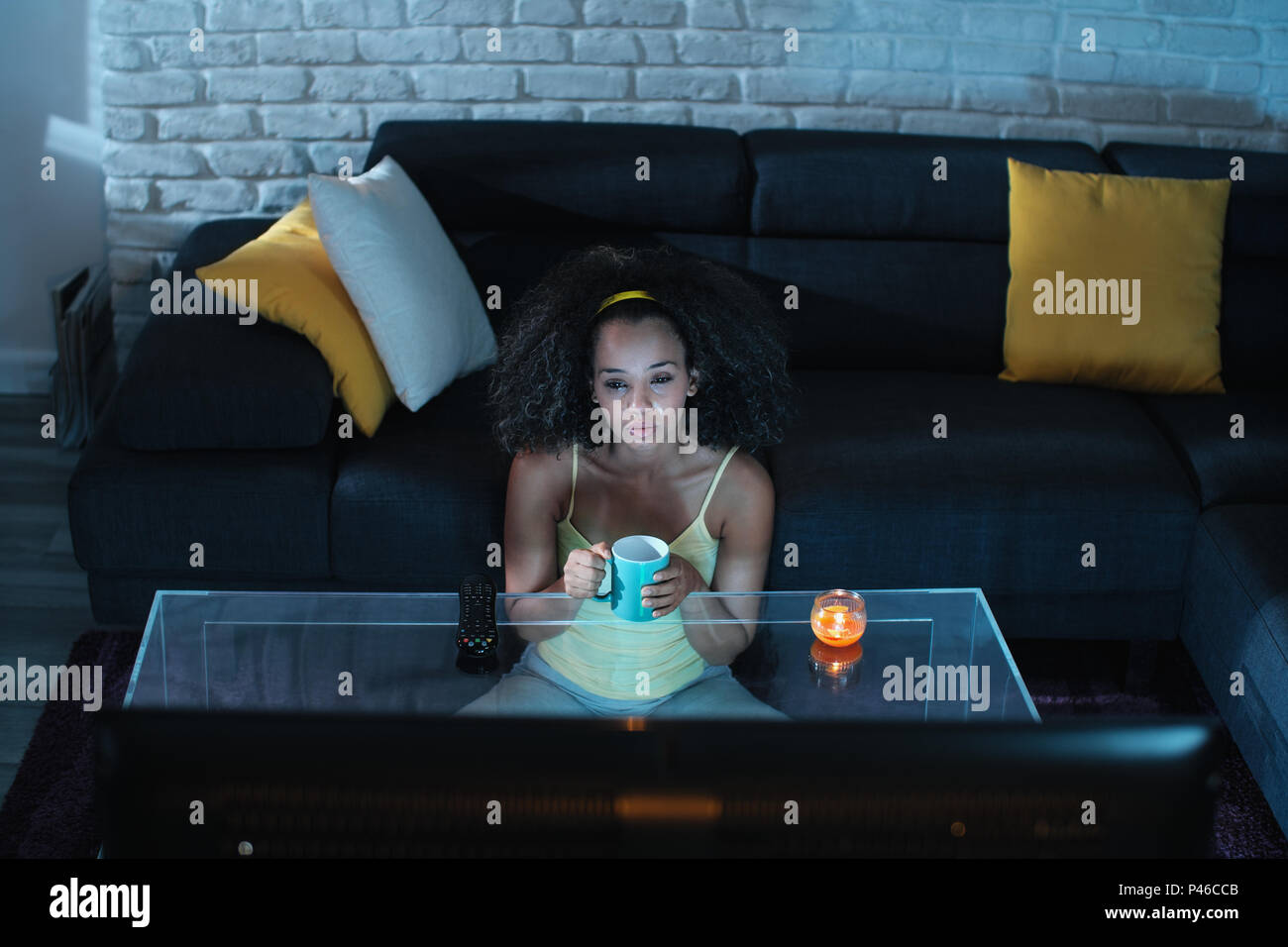 Depressed African American girl alone at home during movie night. Young black woman crying while watching a drama show. Stock Photo