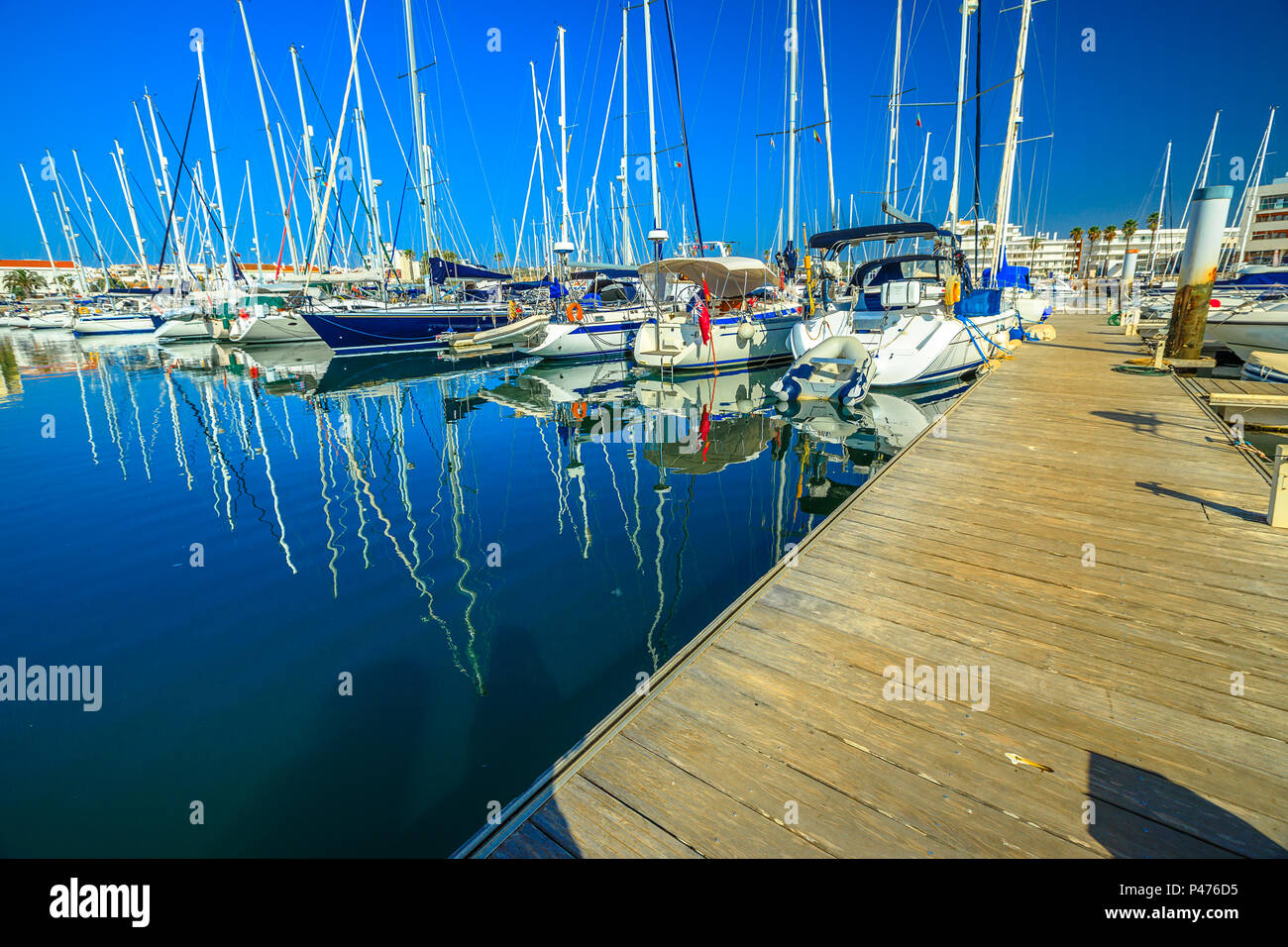 Wooden jetty with sailboats reflected on blue sea in Bay of Lagos. Landscape of Marina de Lagos on Algarve coast, Portugal, Europe. Summer holidays. Stock Photo