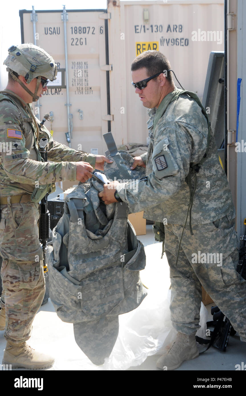 North Carolina Army National Guard Staff Sgt. Christopher Ferguson, a motor transport operator assigned to the 1454th Transportation Company, takes a Improvised Outer Tactical Vest from Spc. James Ward, a wheeled vehicle mechanic assigned to the 1454th TC, before a convoy movement at the Logistics Support Area Forward Operating Base Santa Fe, Fort Irwin, California during the 16-07 National Training Center (NTC) rotation on June 21, 2016. The NTC is a training facility designed to simulate real-life combat scenarios testing warriors’ readiness utilizing their military occupational specialty in Stock Photo