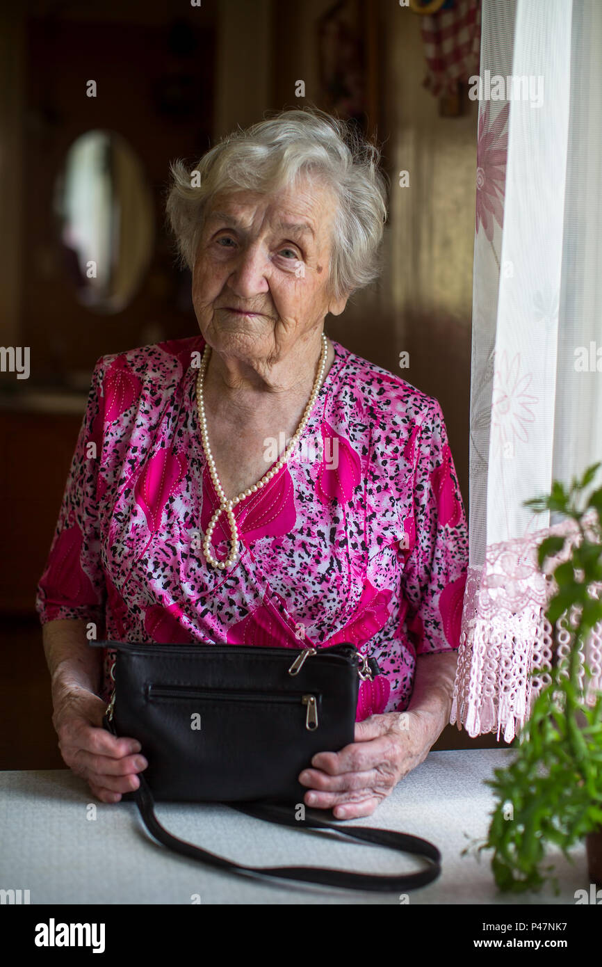 Portrait of an elderly lady with a handbag standing at the table. Stock Photo